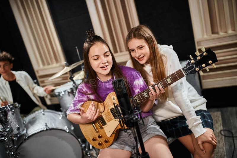 focus on cheerful talented girls playing guitar and singing with their blurred drummer on backdrop, stock photo. focus on cheerful talented girls playing guitar and singing with their blurred drummer on backdrop, stock photo