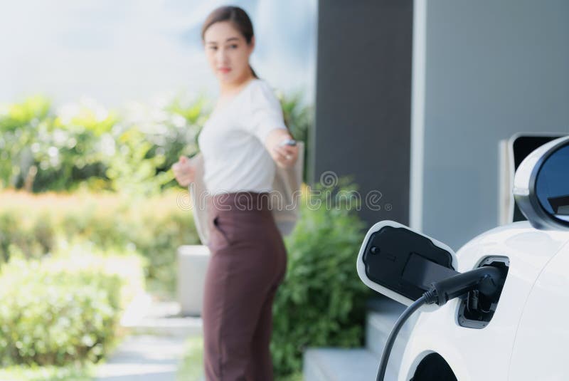 Focus charger plug into EV car with blur backdrop of progressive woman walking.