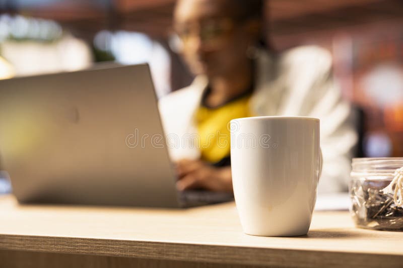 Focus on coffee mug on desk in front of remote worker typing on notebook stock photos