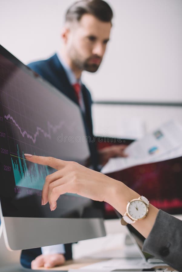 Focus of data analyst pointing on charts on computer monitor near colleague with papers in office royalty free stock images