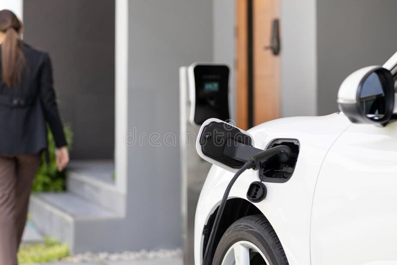 Focus EV car at home charging station with blur progressive woman in the back.