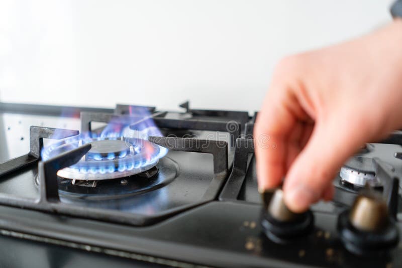 Focus on fire. A man lighting the gas-stove with by means of automatic electric ignition. Modern gas burner and hob on.