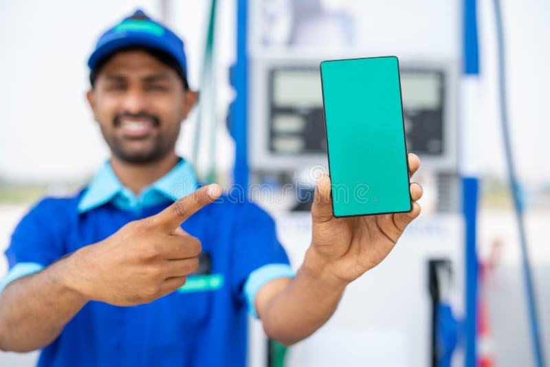 Focus on phone, Smiling petrol pump worker showing green screen mobile phone by pointing finger by looking at camera at