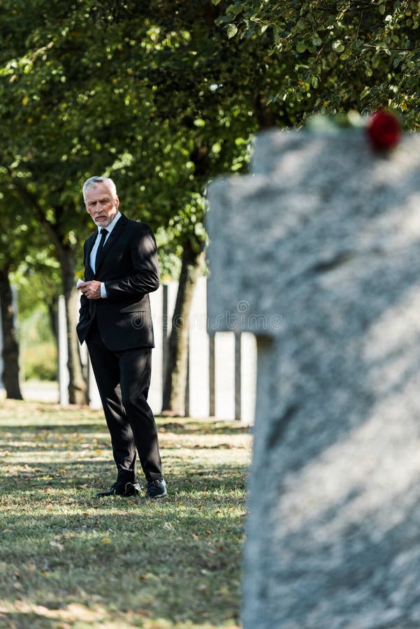 Focus of upset elderly man standing on graveyard stock images