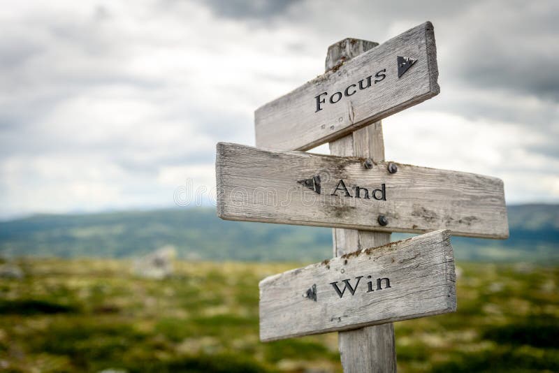 focus and win text engraved on old wooden signpost outdoors in nature