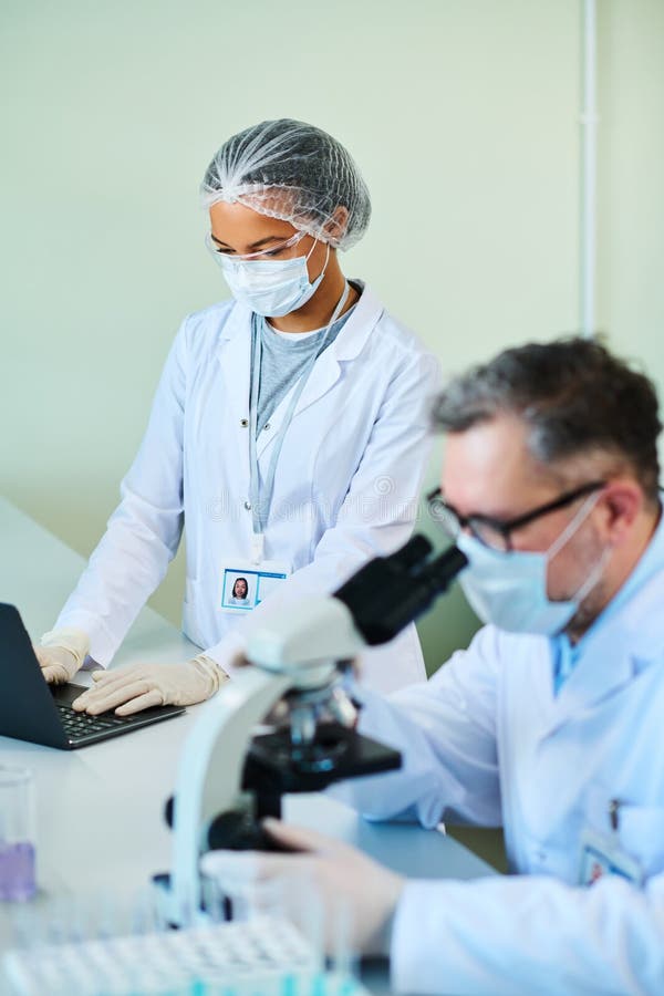 Focus on young female assistant of experienced scientist typing on laptop stock images