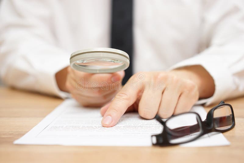 Focused businessman is reading through magnifying glass stock image