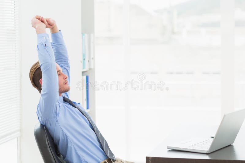 Focused businessman stretching at his desk stock photo
