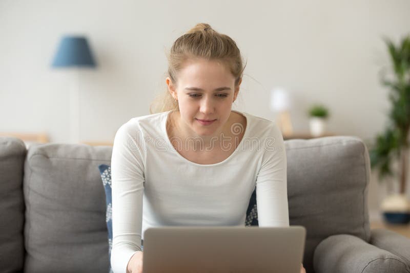 Focused young female using laptop relaxing on couch royalty free stock photo Focused young female using laptop relaxing on couch royalty free stock photo