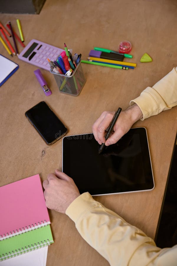Focused image of person using stylus on tablet with surrounding stationery, symbolizing creativity and technology integration. Concept of business, modern technologies, digital art, creative profession