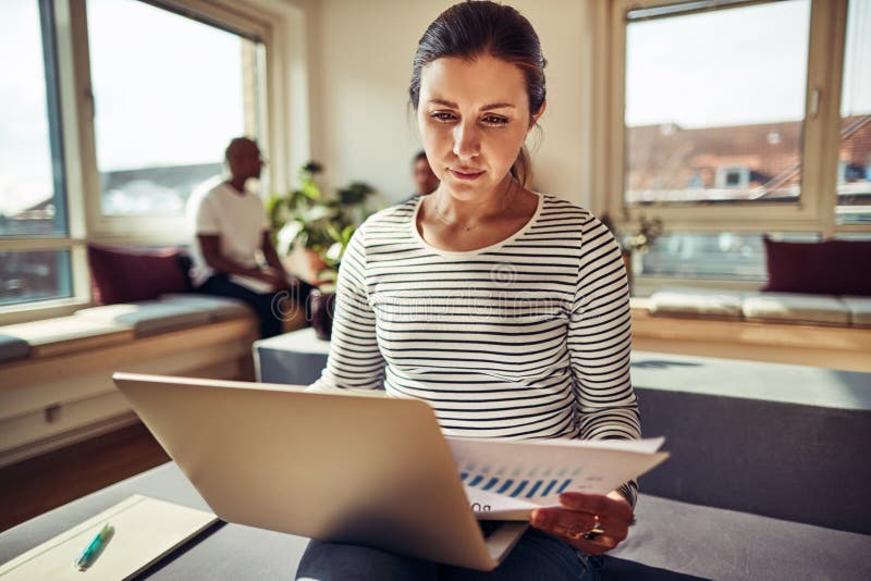 Focused young businesswoman working on a laptop and reading pape stock photos Focused young businesswoman working on a laptop and reading pape stock photos