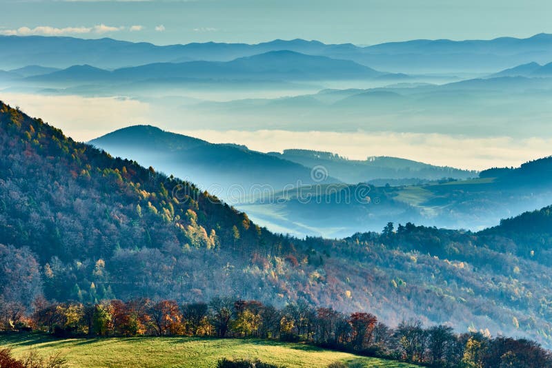 Hmlistá jesenná krajina s horami, slnko prenikajúce cez mraky. Pohľad z vrchu Vršatec, Slovensko.