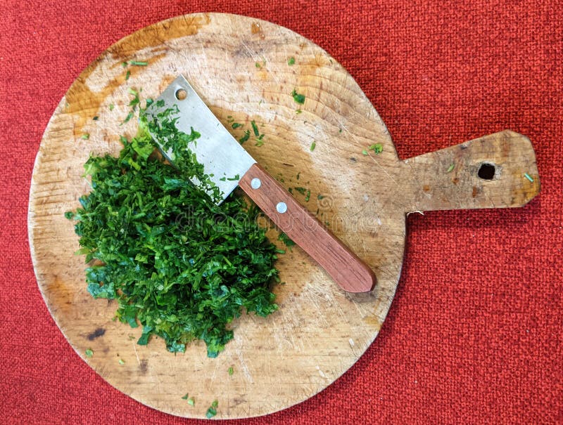 Foglie di prezzemolo fresche su un cartone di legno rotondo. Foglie fresche di prezzemolo su un pannello di legno rotondo e coltello versatile con lama larga utilizzata nella cottura cinese