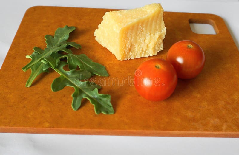 Foglie, pomodori ciliegia e parmigiano verdi freschi della rucola su pannello rigido fotografie stock libere da diritti Foglie, pomodori ciliegia e parmigiano verdi freschi della rucola su pannello rigido fotografie stock libere da diritti