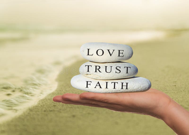 Hands holding a stack of pebbles with 'faith, trust and love' written on the top stone. Hands holding a stack of pebbles with 'faith, trust and love' written on the top stone.