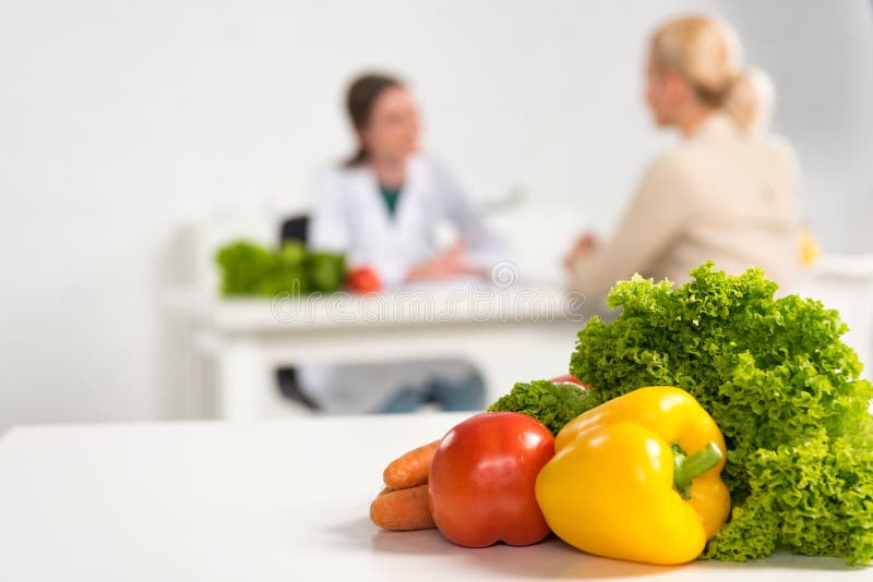 Fokus på dietitisen i vit rock och patienten vid bord och färska grönsaker på förgrund fotografering för bildbyråer