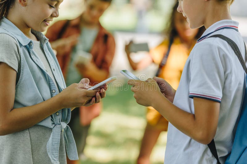 Fokus på skolbarn som använder smarta telefoner medan de står nära mångkulturella vänner arkivfoto