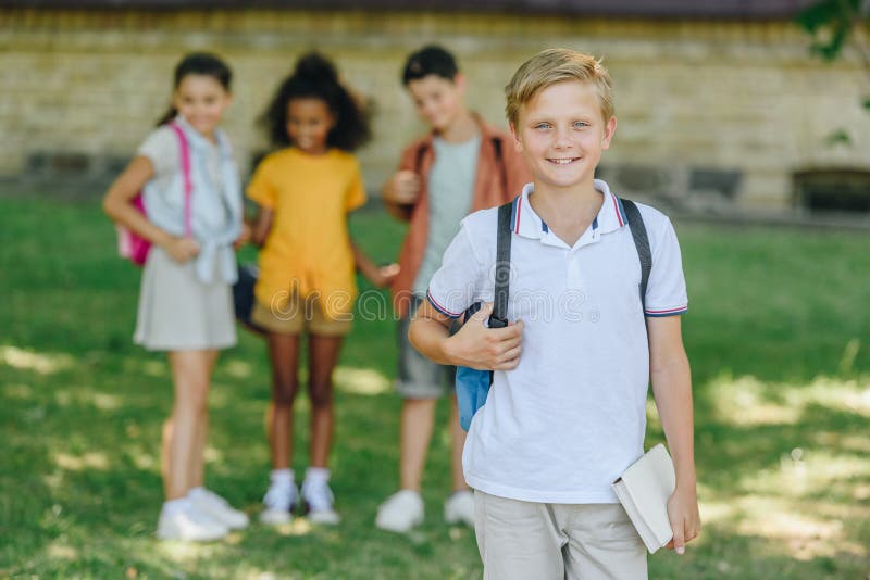 Fokus på söt skolpojke som leker inom stängda dörrar medan man står nära multietniska vänner arkivbild