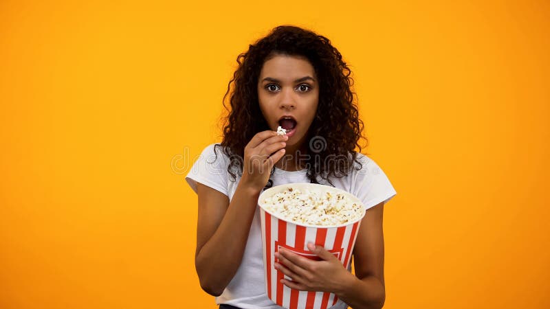 Fokussierte afro-amerikanische Frau, die Popcorn isst und interessante Show aufpasst lizenzfreies stockfoto Fokussierte afro-amerikanische Frau, die Popcorn isst und interessante Show aufpasst lizenzfreies stockfoto