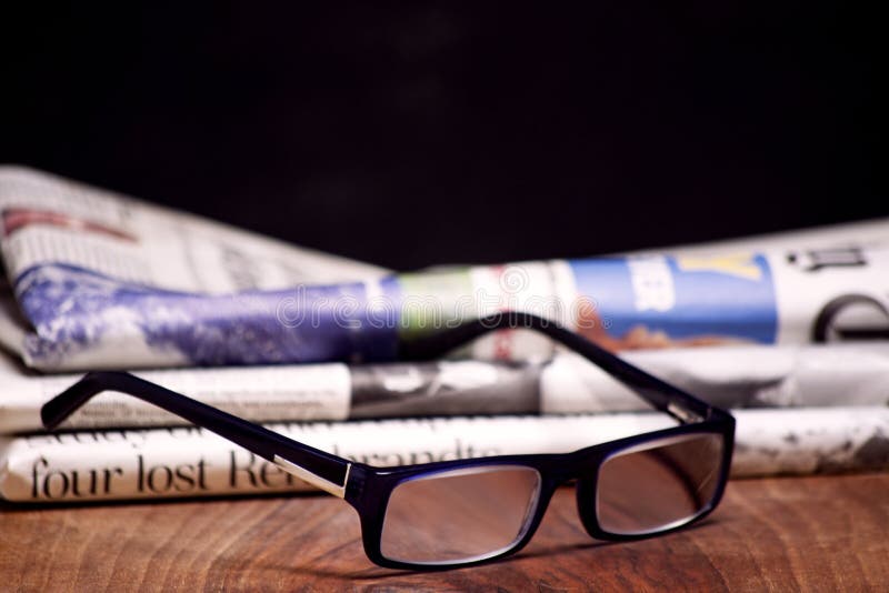 Folded Newspaper with a Pair of Blue Reading Glasses on it Stock Image