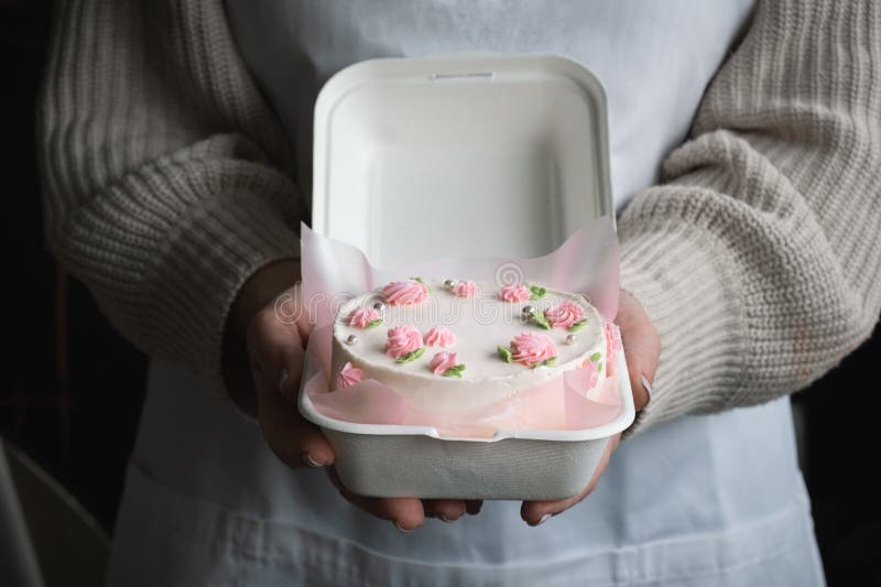 Chef de pastelaria feminino mantém um bolo decorado com flores sobre fundo  branco