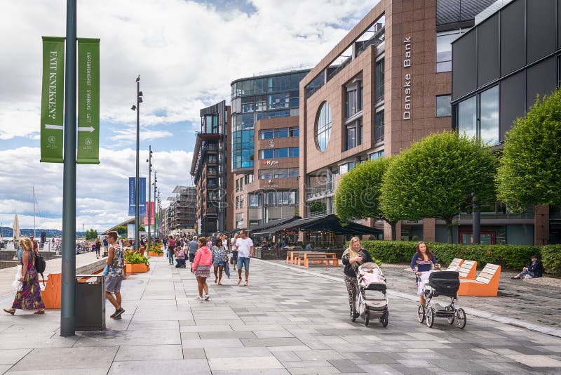 Folk som tycker om sommarsolskenet bredvid alfreskomålningrestaurangerna och de moderna hyreshusarna av Aker Brygge royaltyfri fotografi Folk som tycker om sommarsolskenet bredvid alfreskomålningrestaurangerna och de moderna hyreshusarna av Aker Brygge royaltyfri fotografi