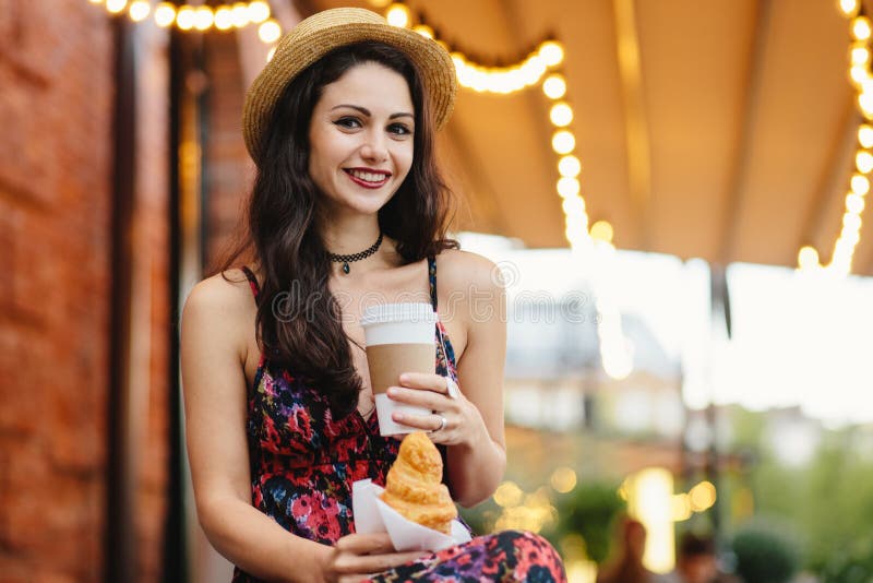 Folket mat, vilar och livsstilbegrepp Brunettkvinna med långt hår, den bärande sommarklänningen och hatten som dricker takeaway k fotografering för bildbyråer Folket mat, vilar och livsstilbegrepp Brunettkvinna med långt hår, den bärande sommarklänningen och hatten som dricker takeaway k fotografering för bildbyråer