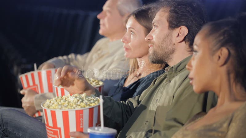 Folket rymmer hinkar med popcorn i deras händer på filmbiografen