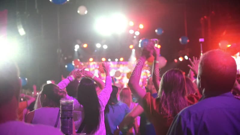 Folkmassa av folk som dansar som lyfter händer på en konsert - mång--färgade ballonger som flyger runt om konserthallen