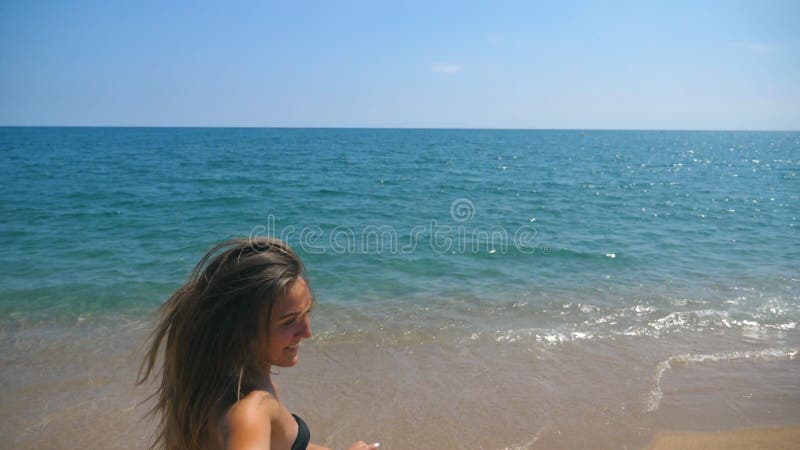 Follow me shot of young woman pull her boyfriend to the sea shore. Beautiful girl holding male hand and running on