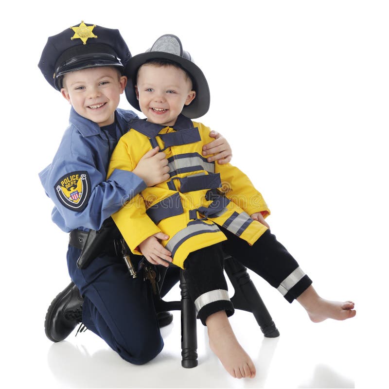 Little brothers posing together, the little one dressed as a fireman, the older his big brother dressed as a policeman. On a white background. Little brothers posing together, the little one dressed as a fireman, the older his big brother dressed as a policeman. On a white background