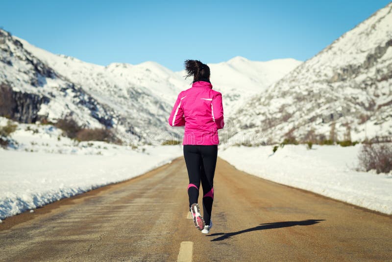 Woman running in cross country road on winter. Rear view of female runner training for marathon in snowy mountains landscape. Woman running in cross country road on winter. Rear view of female runner training for marathon in snowy mountains landscape.