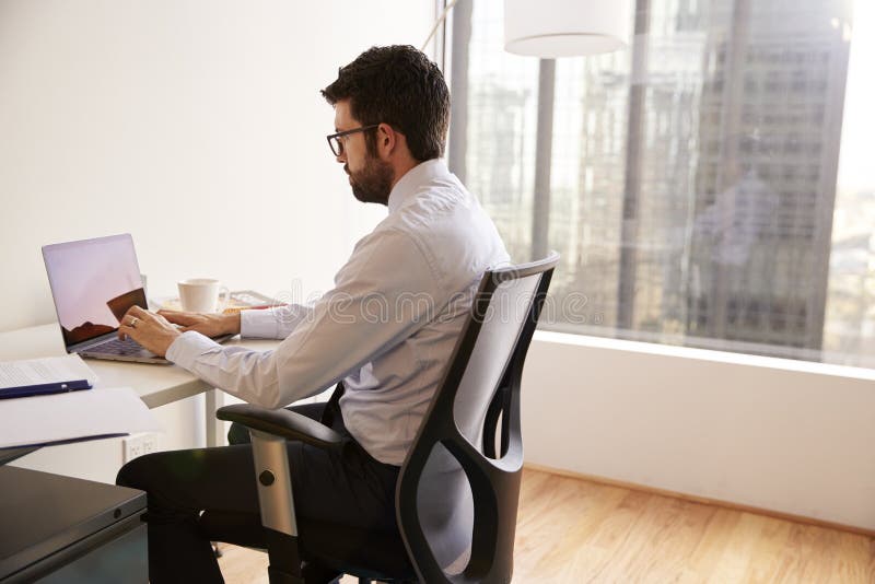 Fonctionnement de Sitting At Desk d'homme d'affaires sur l'ordinateur portable dans le bureau moderne images stock Fonctionnement de Sitting At Desk d'homme d'affaires sur l'ordinateur portable dans le bureau moderne images stock