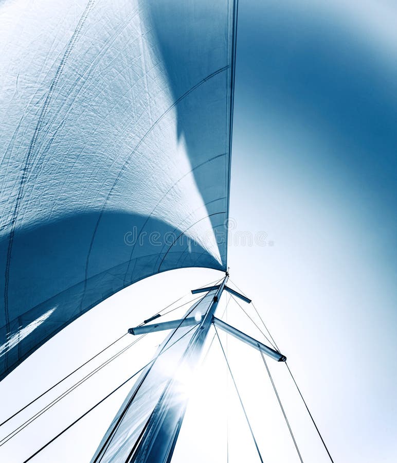 Sailboat in action, big white sail raised over blue clear sky, luxury leisure, summertime activities and extreme sport, boat parts with sun rays, sailing trip vacation, freedom concept. Sailboat in action, big white sail raised over blue clear sky, luxury leisure, summertime activities and extreme sport, boat parts with sun rays, sailing trip vacation, freedom concept