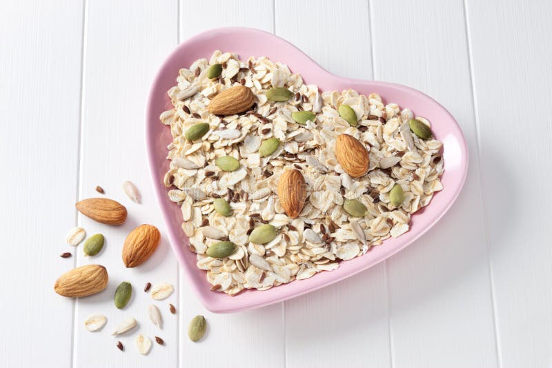 A heart shaped bowl full of muesli, with oats, almonds and grains on a white background. A heart shaped bowl full of muesli, with oats, almonds and grains on a white background