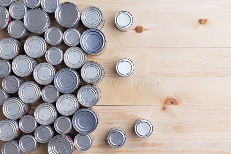 Conceptual background of multiple canned foods for food drive donations in sealed aluminum tins or cans of varying sizes arranged on a wooden table with copy space, overhead view. Conceptual background of multiple canned foods for food drive donations in sealed aluminum tins or cans of varying sizes arranged on a wooden table with copy space, overhead view.