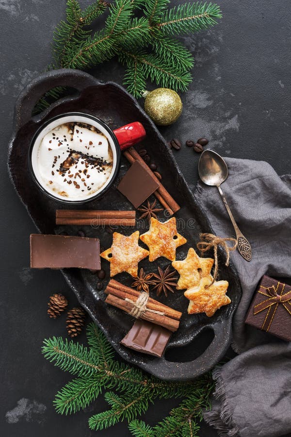 Fondo de la Navidad con el chocolate caliente en una taza roja con las melcochas, las galletas, las especias y el chocolate en un foto de archivo Fondo de la Navidad con el chocolate caliente en una taza roja con las melcochas, las galletas, las especias y el chocolate en un foto de archivo