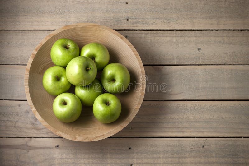 A wood bowl full of green apples on a rustic wood background. A wood bowl full of green apples on a rustic wood background