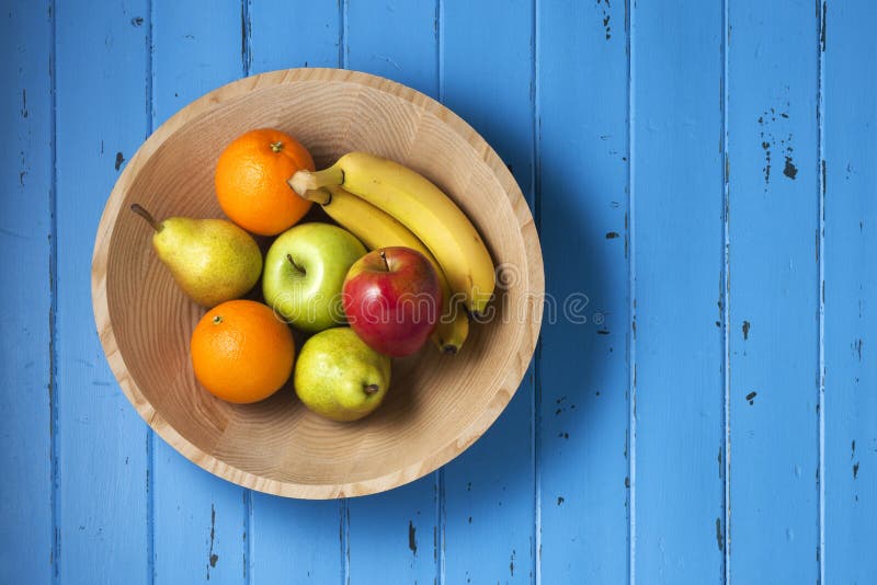 A wood bowl of fruit on a blue painted wood background. A wood bowl of fruit on a blue painted wood background