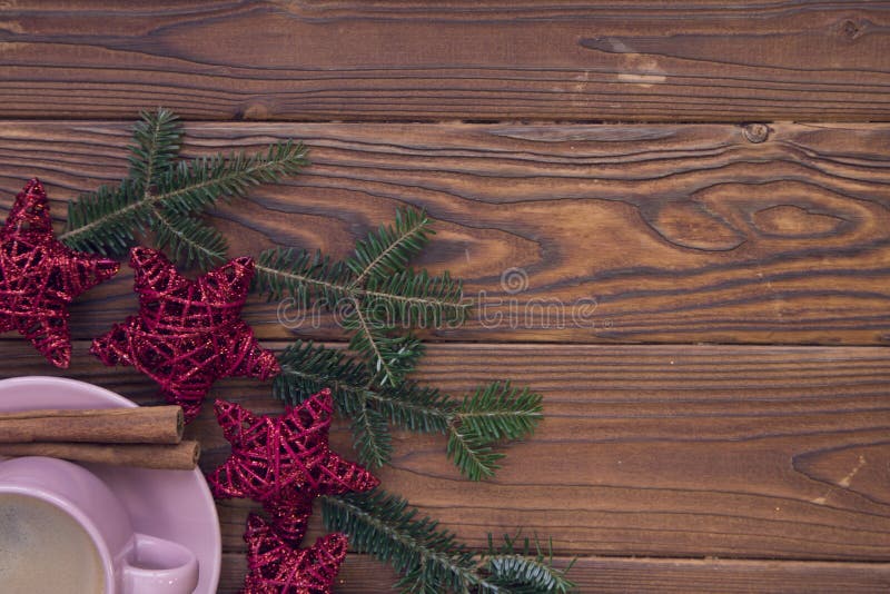 Fondo de madera rústico de la Navidad con las ramas y el café de árbol de abeto. Fondo de madera rústico de la Navidad con las ramas de árbol de abeto Un cappuchino caliente en una taza porcelian rosada con los palillos del canela en un platillo, brillo rojo protagoniza Visión superior Cierre para arriba Copyspace