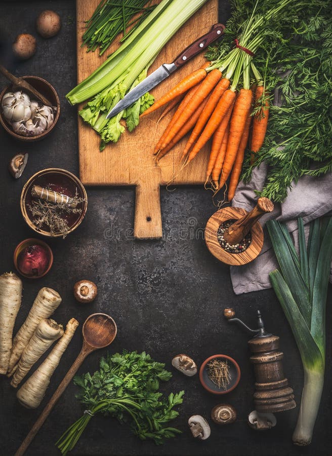 Fondo dell'alimento con le varie verdure organiche dell'azienda agricola sulla tavola rustica scura con gli utensili della cucina immagini stock Fondo dell'alimento con le varie verdure organiche dell'azienda agricola sulla tavola rustica scura con gli utensili della cucina immagini stock