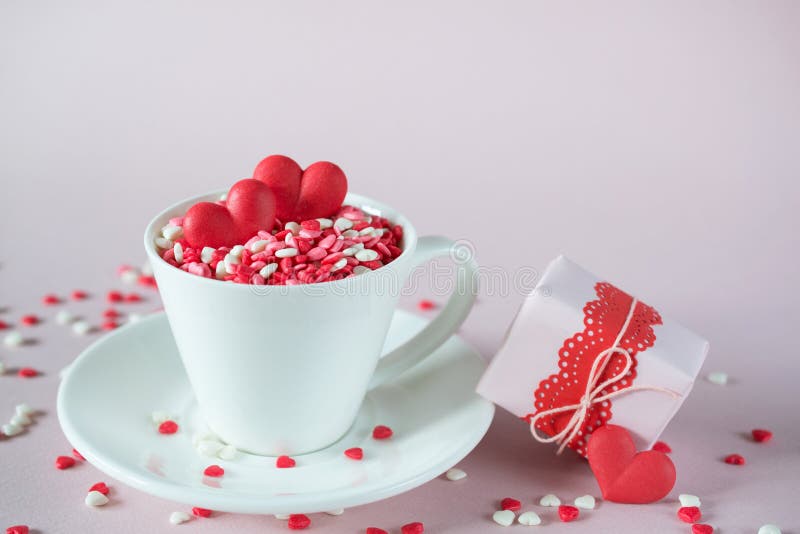Fondo festivo La taza de café, llena de dulce multicolor asperja corazones del caramelo de azúcar y el regalo del día del ` s de imagen de archivo libre de regalías Fondo festivo La taza de café, llena de dulce multicolor asperja corazones del caramelo de azúcar y el regalo del día del ` s de imagen de archivo libre de regalías