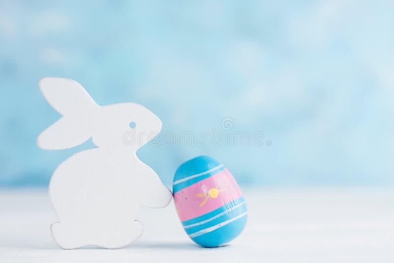 Fondo luminoso di Pasqua: coniglietto di legno bianco con l'uovo paited contro la parete blu Concetto di festa fotografie stock Fondo luminoso di Pasqua: coniglietto di legno bianco con l'uovo paited contro la parete blu Concetto di festa fotografie stock