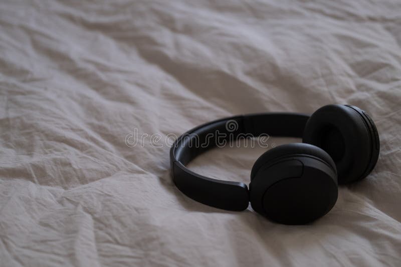 Fones de ouvido pretos sem fio deitados sobre camas de bege à luz natural. fotografia de stock