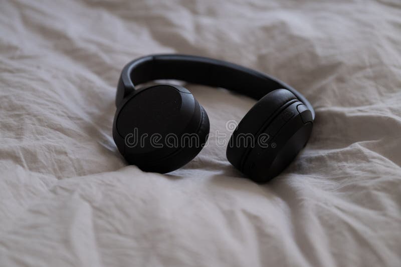 Fones de ouvido pretos sem fio deitados sobre camas de bege à luz natural. imagens de stock