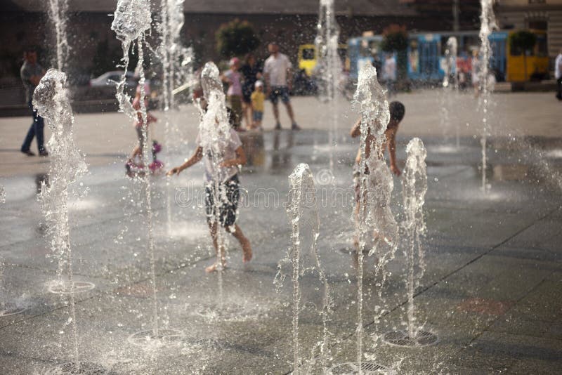 Fontana della città nel calore di estate Bambini che corrono fra gli scorrimenti dell'acqua fotografia stock Fontana della città nel calore di estate Bambini che corrono fra gli scorrimenti dell'acqua fotografia stock