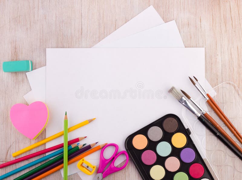 Top view of white blank paper with water colors and other school supplies on wooden desk. Art and craft concept. Top view of white blank paper with water colors and other school supplies on wooden desk. Art and craft concept