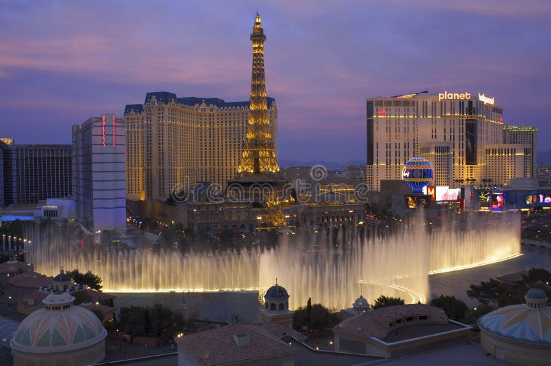 A view from the Bellagio Hotel of the Bellagio fountains and the famous Strip. In the background the are several hotels and a replica of the Eiffel Tower. The sun is setting and there is a pink tinge to the thin clouds. A view from the Bellagio Hotel of the Bellagio fountains and the famous Strip. In the background the are several hotels and a replica of the Eiffel Tower. The sun is setting and there is a pink tinge to the thin clouds.