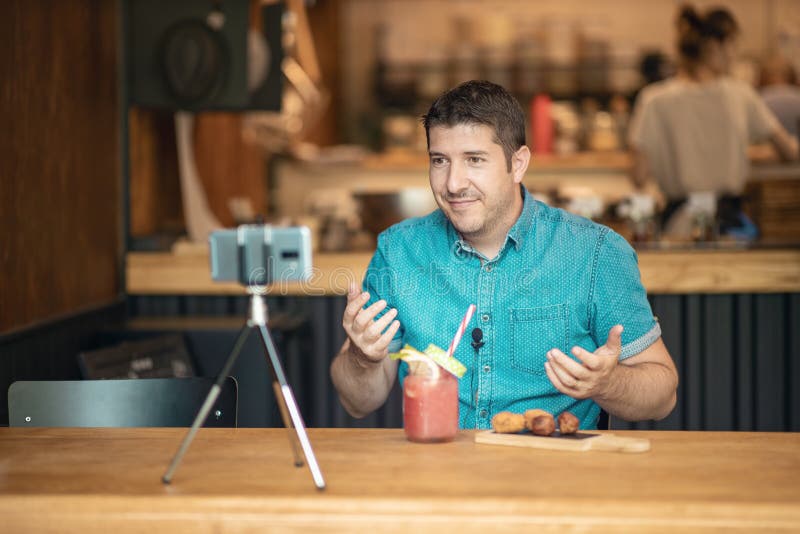 Food blogger streaming live on social media - Man creating blog video content using smart phone camera on a tripod stock image Food blogger streaming live on social media - Man creating blog video content using smart phone camera on a tripod stock image