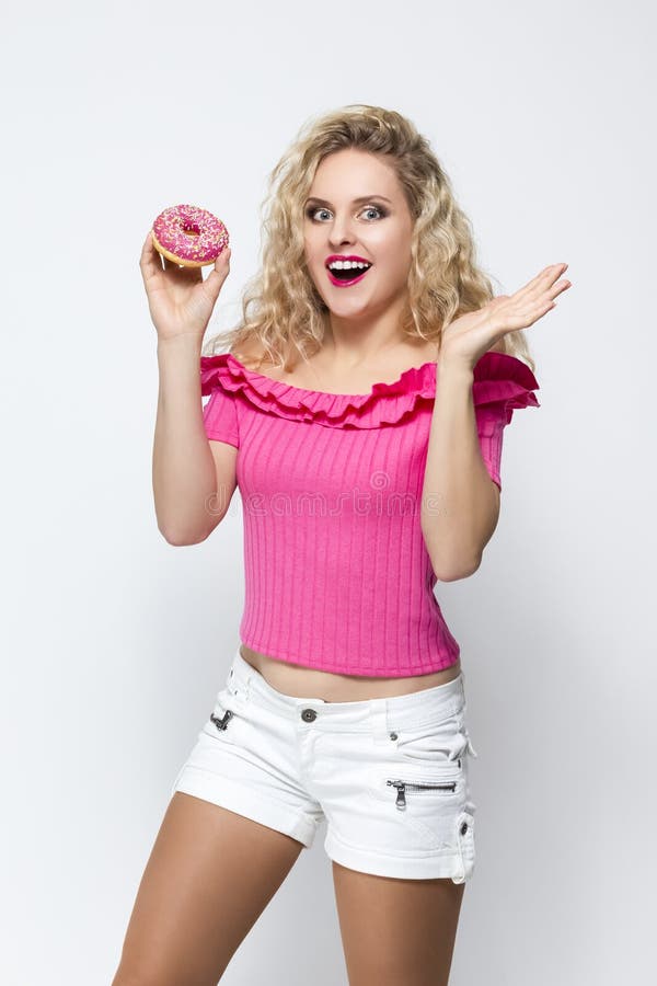 Food Concepts. Cute and Funny  Caucasian Blond Girl With Pink Doughnut in Hands. Posing With Excited Facial Expression. Standing